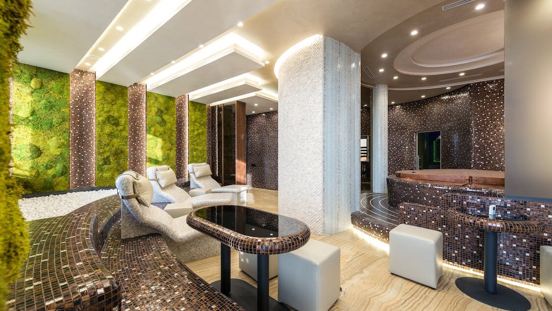Modern indoor spa lounge with curved tiled seating, water features, soft lighting, and relaxation tables